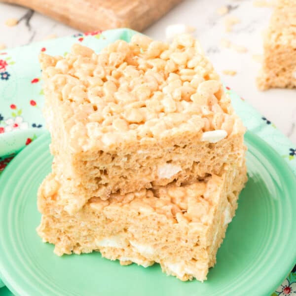 Square crop of two thick, gooey Browned Butter Rice Crispy Treats stacked on a green plate with visible marshmallow pockets.