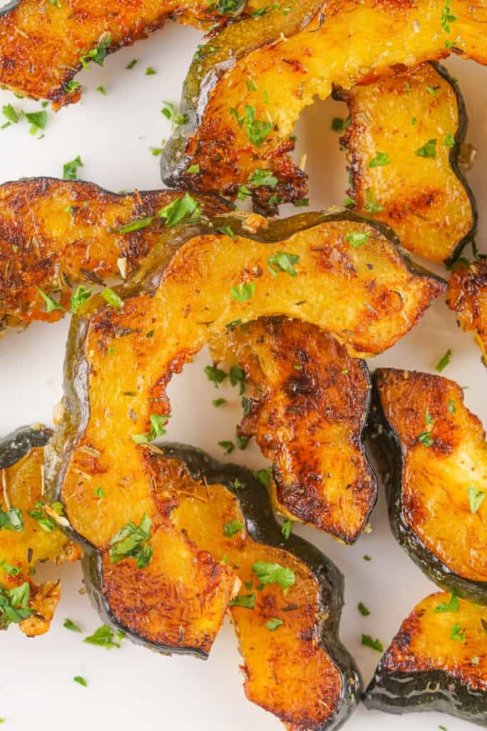 Overhead view of golden roasted acorn squash slices garnished with parsley on a white plate.