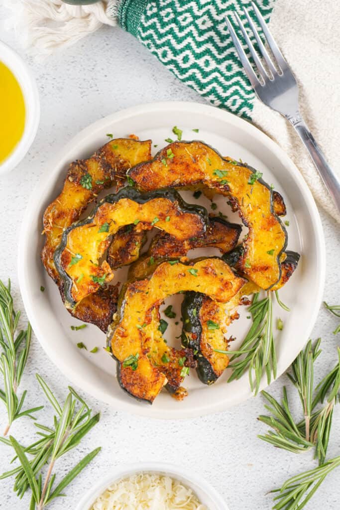 Plate of roasted acorn squash slices arranged in a circle with rosemary sprigs and a fork.