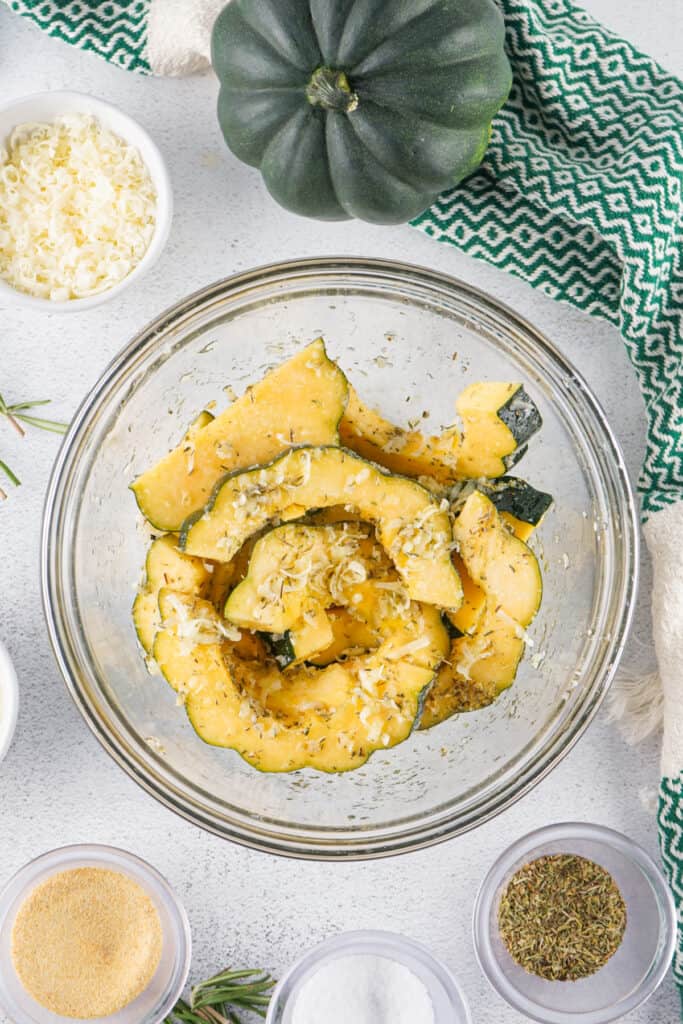 Mixing bowl filled with sliced acorn squash tossed with cheese and seasonings before roasting.