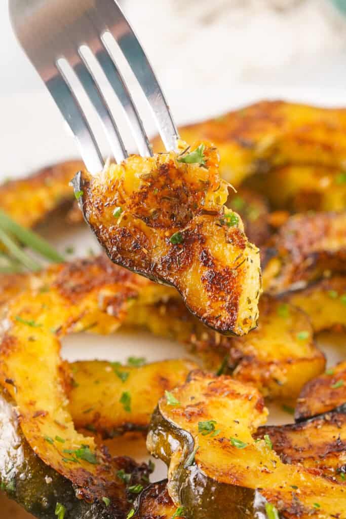 Close-up of a fork holding a bite of roasted acorn squash topped with herbs and parmesan.