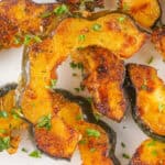 Close-up of roasted acorn squash slices with golden edges and parsley garnish on a white plate.