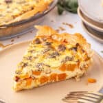 Square cropped photo of roasted squash quiche slice on a beige plate, with golden phyllo edges and visible chunks of butternut squash.
