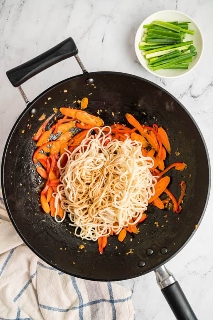 Lo mein sauce poured over the noodles and vegetables in the wok, ready to be mixed.