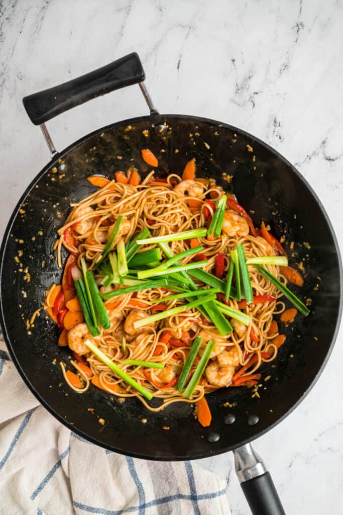 Green onions added on top of the shrimp lo mein in a wok before final mixing.