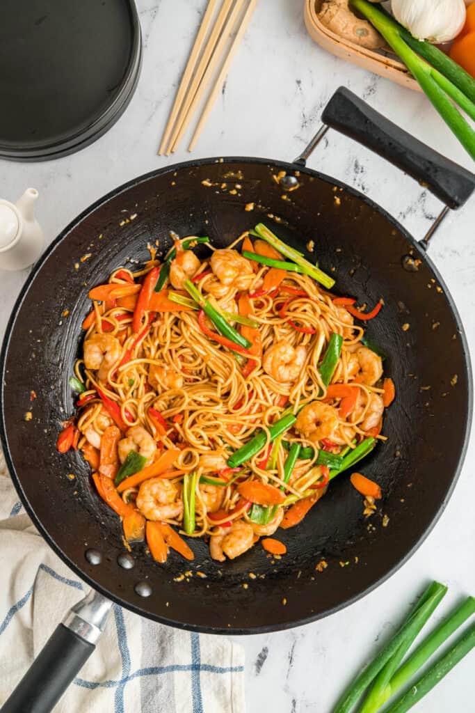 Finished shrimp lo mein in a wok with shrimp, vegetables, and noodles coated in sauce.