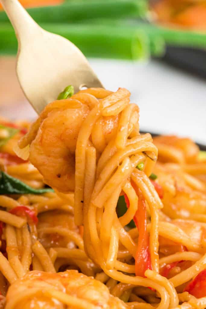 Close-up of a fork twirling noodles and shrimp coated in sauce.