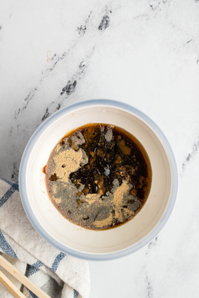 Lo mein sauce in a bowl with white pepper and other spices sprinkled on top before mixing.