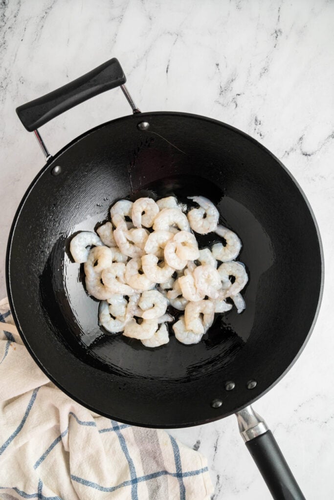 Raw shrimp in a black wok with oil, beginning to cook for shrimp lo mein.