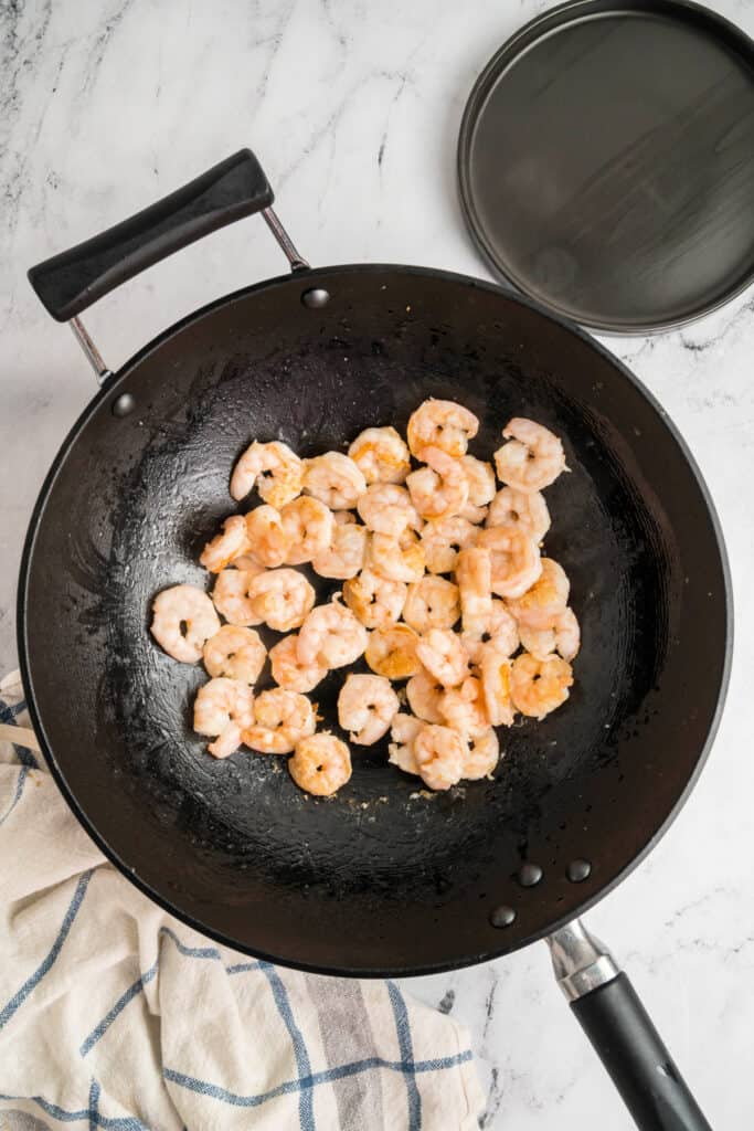 Shrimp cooking in a wok until pink and lightly browned.