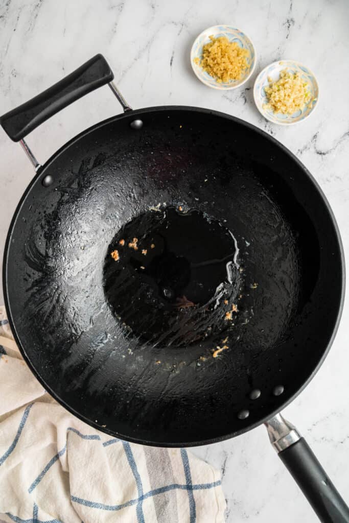 Empty wok with oil and bits of garlic and ginger left after cooking shrimp.