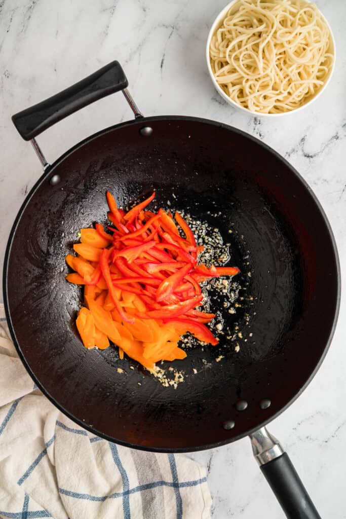 Carrots and red bell pepper strips added to the wok with garlic and ginger.