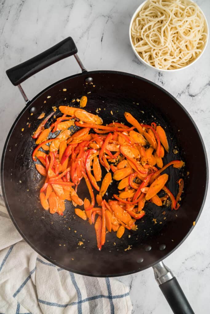 Sautéed carrots and red bell peppers cooking in the wok with garlic and ginger.