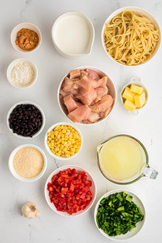 Overhead view of ingredients for southwest chicken fettuccine alfredo with pasta, chicken, peppers, beans, corn, and cream.