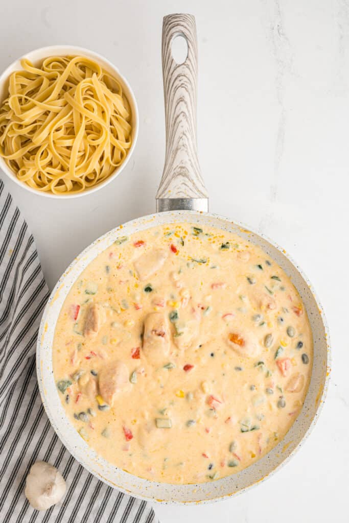 Sauce simmering with chicken, beans, and corn combined.