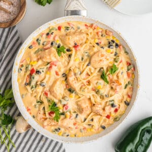 Overhead square crop of skillet filled with southwest chicken fettuccine alfredo, garnished with parsley.