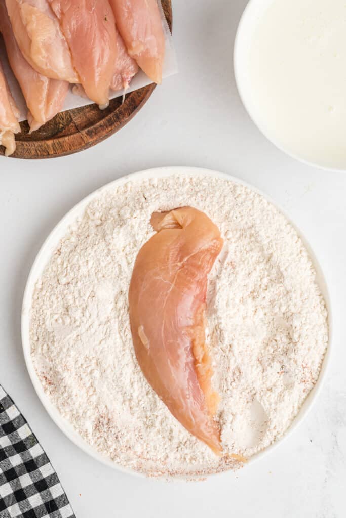 Raw chicken tenderloin being dredged in seasoned flour for southwest chicken tenders.