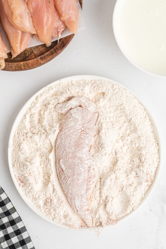 Raw chicken tenderloin fully coated in seasoned flour mixture before dipping in buttermilk.