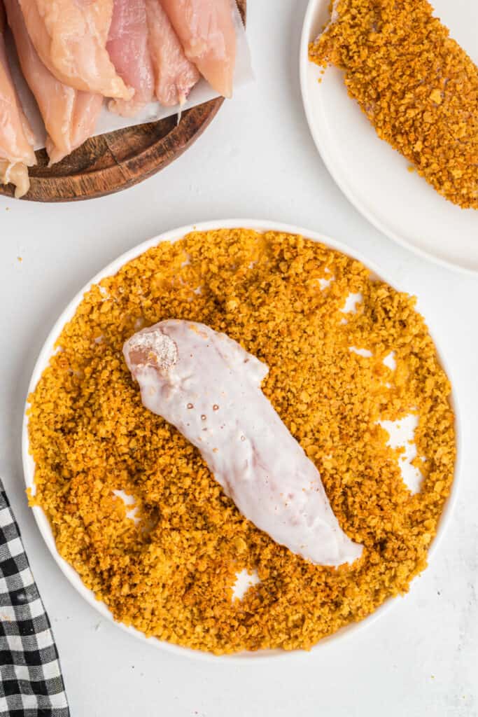 Buttermilk-coated chicken tenderloin placed in seasoned corn chip crumbs.
