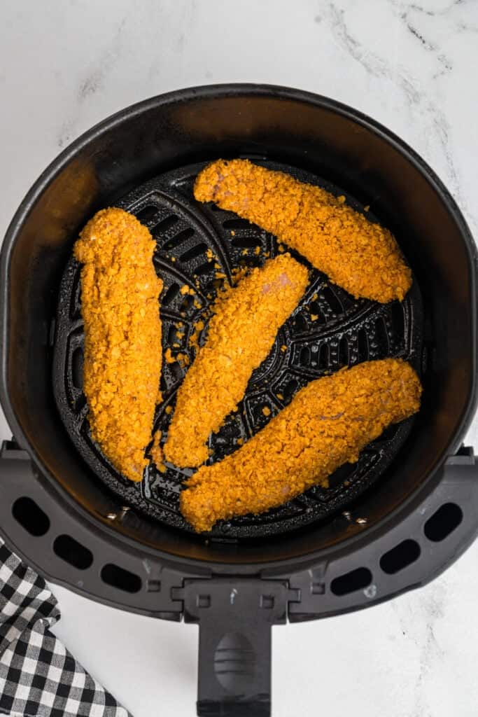 Breaded chicken tenders arranged in the air fryer basket before cooking.