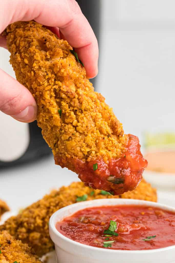 Hand dipping a crispy southwest chicken tender into a bowl of salsa.