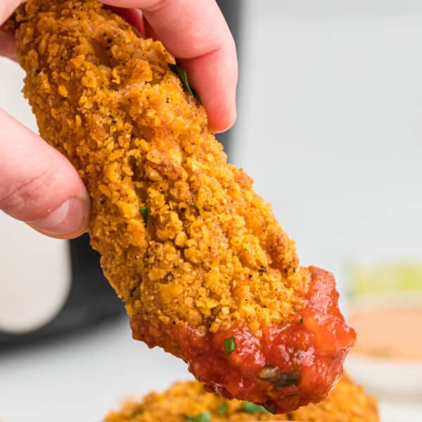 Close-up square photo of a hand dipping a southwest chicken tender into salsa.