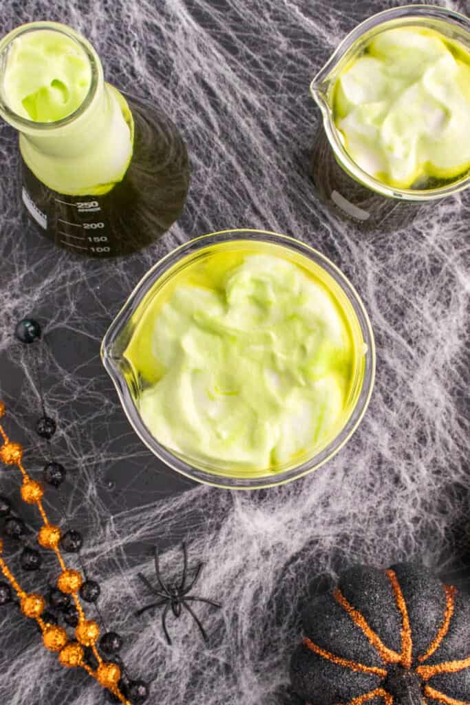 Beakers of Toxic Waste Punch topped with green foamy whipped cream swirled on top for a spooky bubbling effect.