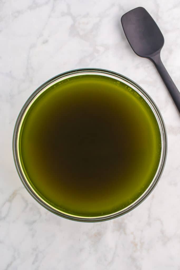 Large glass bowl of dark green punch after food coloring is added, with a black spatula and green food coloring bottle on the side.