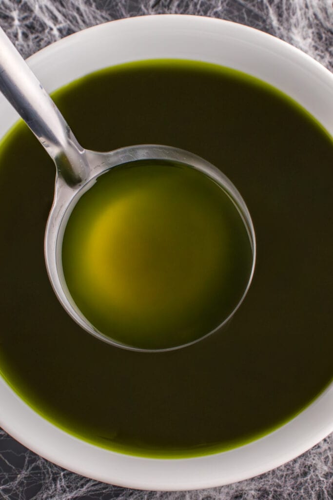 Ladle dipping into a bowl of dark green Toxic Waste Punch on a Halloween-themed table with cobweb decorations.