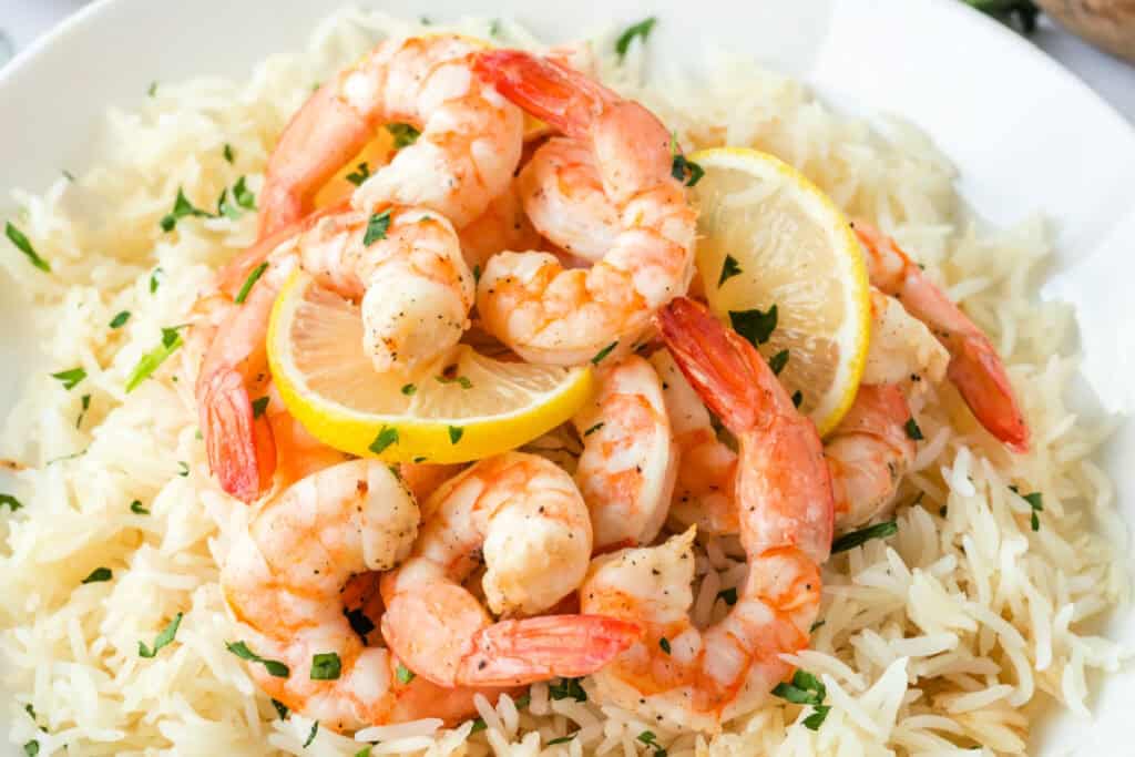 Air Fryer Shrimp served over a bed of white rice with lemon slices and parsley garnish.