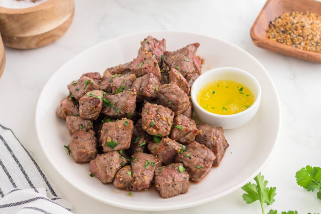 Plate of juicy air fryer steak bites garnished with parsley and served with melted garlic butter dip.