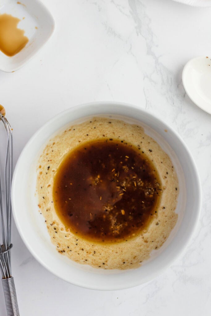 Bowl of steak marinade made with olive oil, soy sauce, honey, and seasoning on a marble countertop.