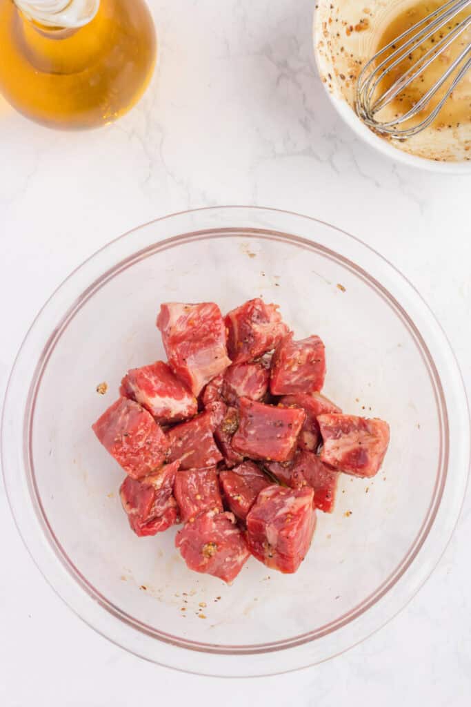 Steak cubes in a glass bowl coated with savory marinade, ready to be cooked in the air fryer.