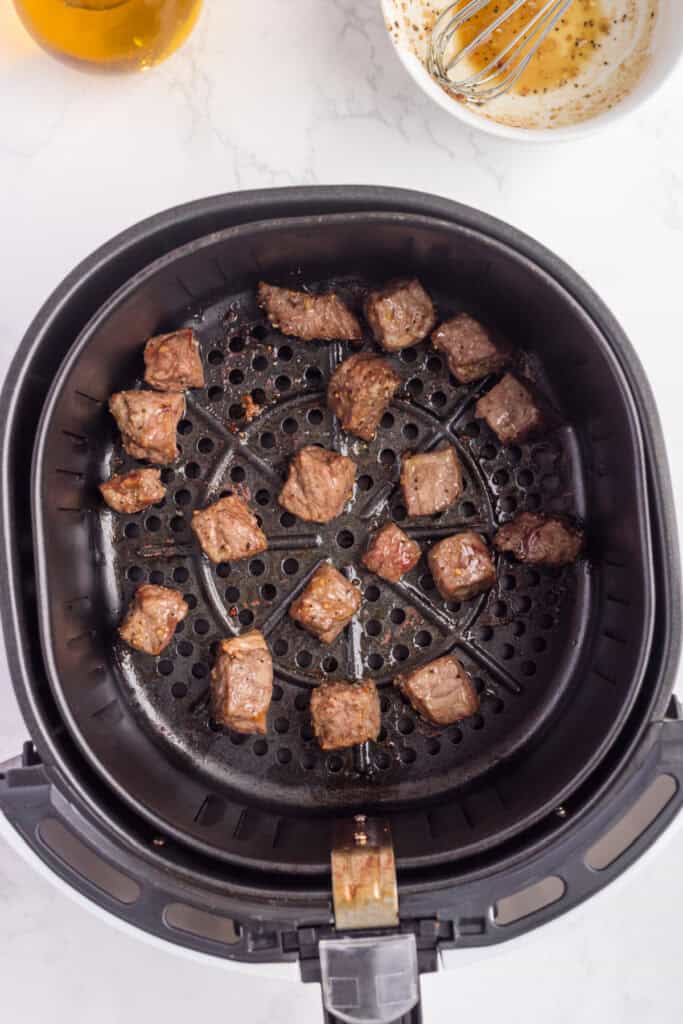 Cooked steak bites in the air fryer basket, browned on the outside and juicy on the inside.