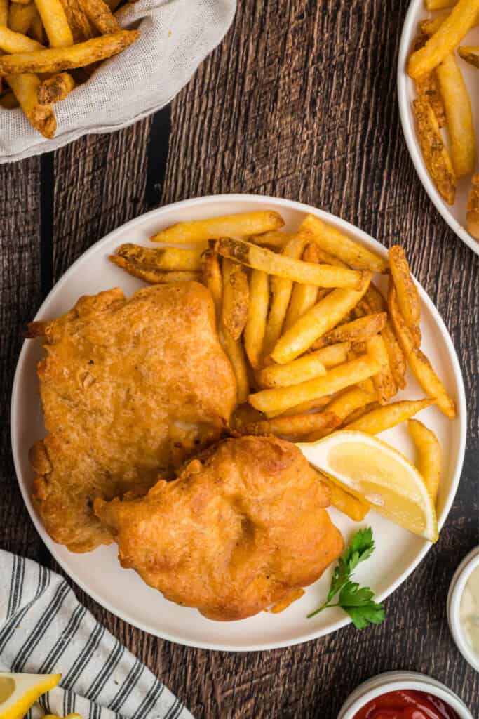 Overhead shot of golden fried beer battered fish and fries with dipping sauces on a rustic wood table.