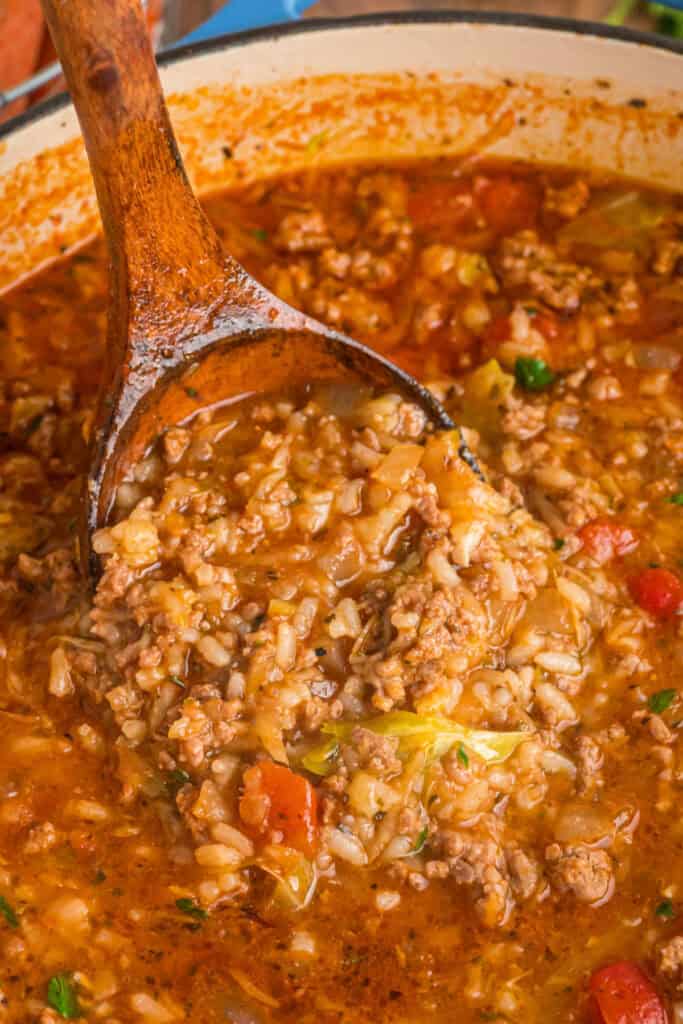 Wooden ladle lifting a hearty scoop of cabbage roll soup filled with rice, beef, tomatoes, and cabbage.
