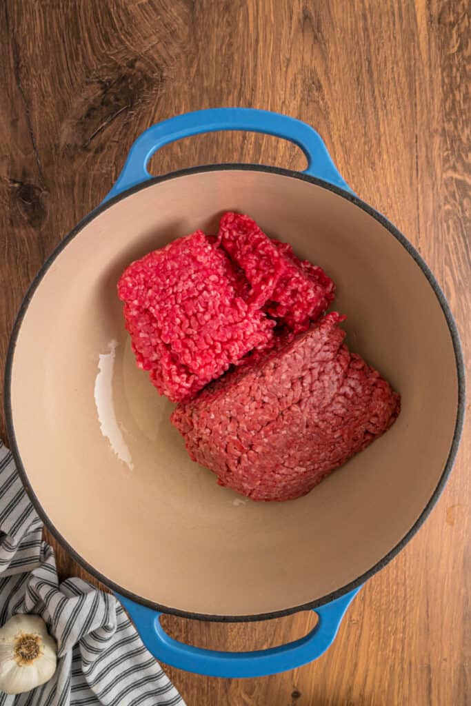 Raw ground beef and pork in a large blue dutch oven before cooking.
