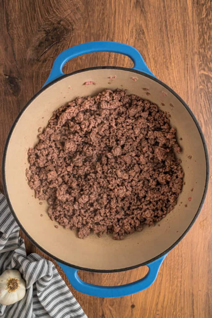 Cooked and crumbled ground beef and pork in a blue dutch oven after browning.