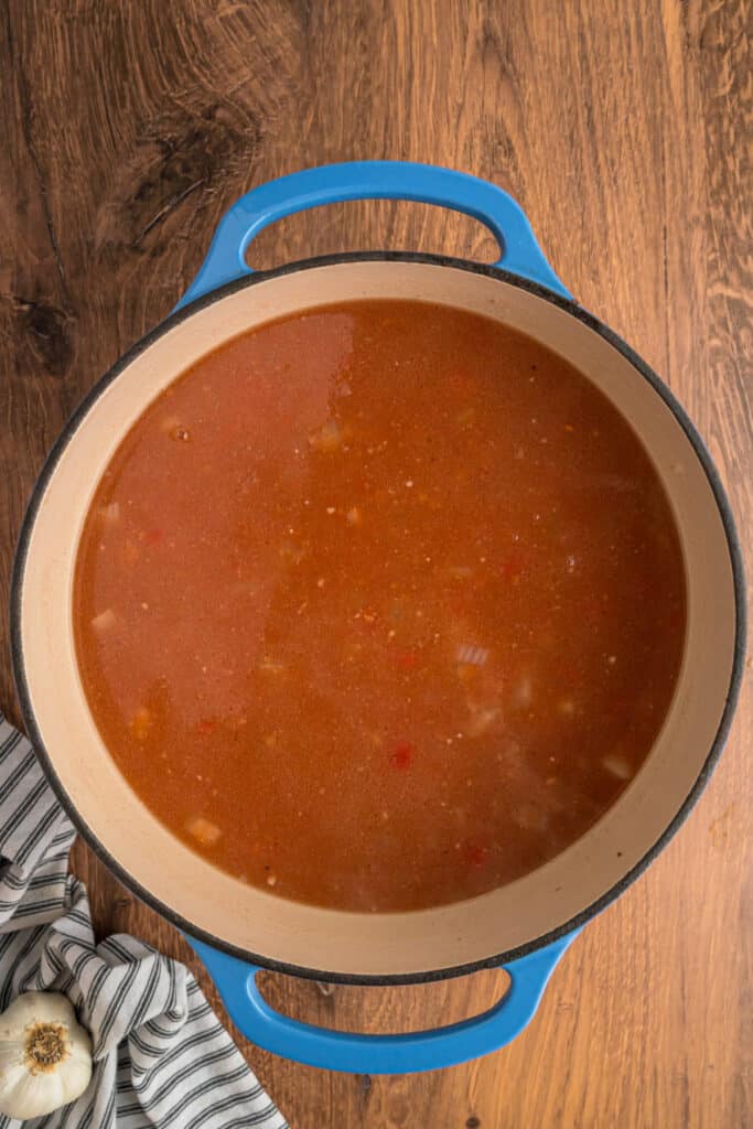 Simmering tomato broth mixture for cabbage roll soup in a blue dutch oven.