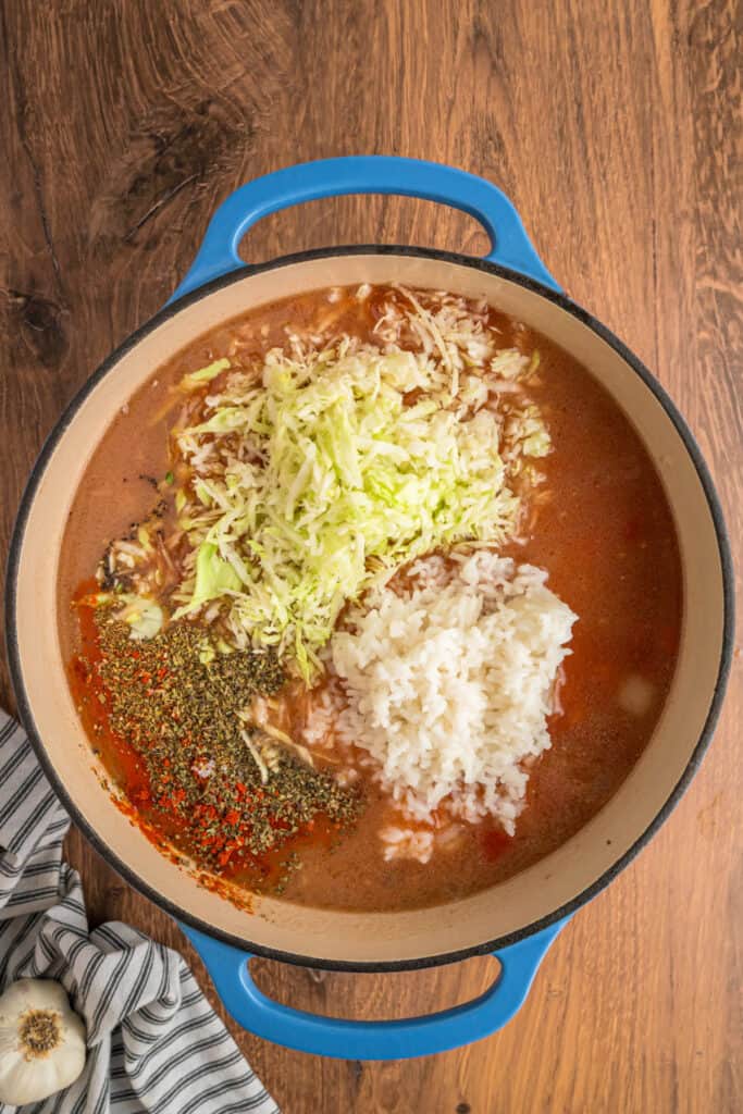 Shredded cabbage, cooked rice, and seasonings added to the soup base before stirring.