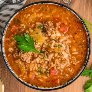 Overhead close-up of a bowl of cabbage roll soup topped with parsley, showing rice, beef, cabbage, and tomato broth.