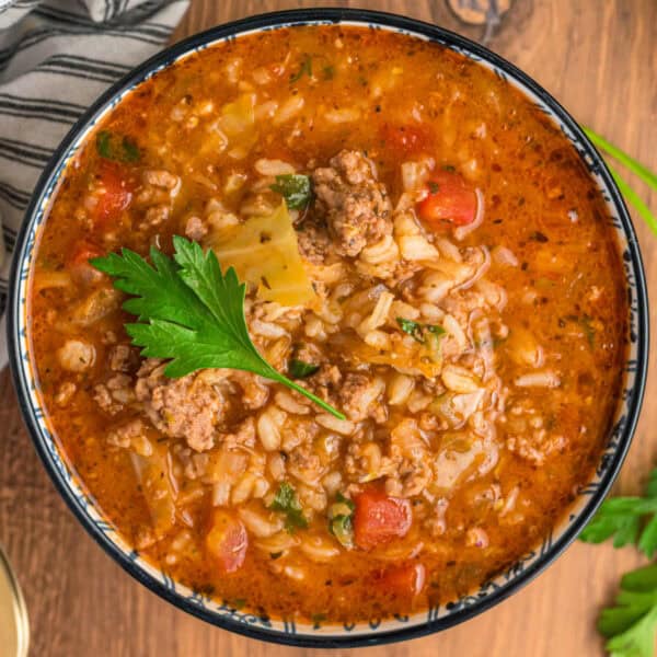 Overhead close-up of a bowl of cabbage roll soup topped with parsley, showing rice, beef, cabbage, and tomato broth.