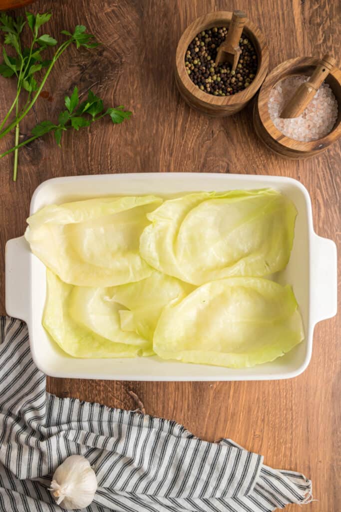 Layer of blanched cabbage leaves arranged in the bottom of a white baking dish to create a base.