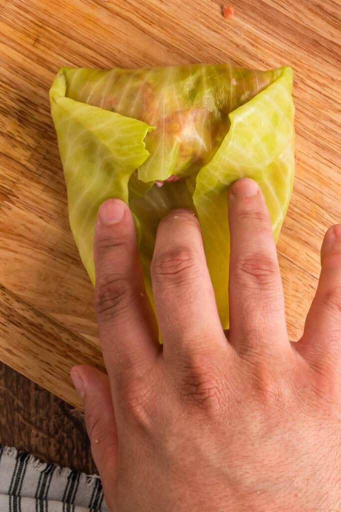 Hands folding sides of the cabbage leaf inward to secure the filling while rolling.