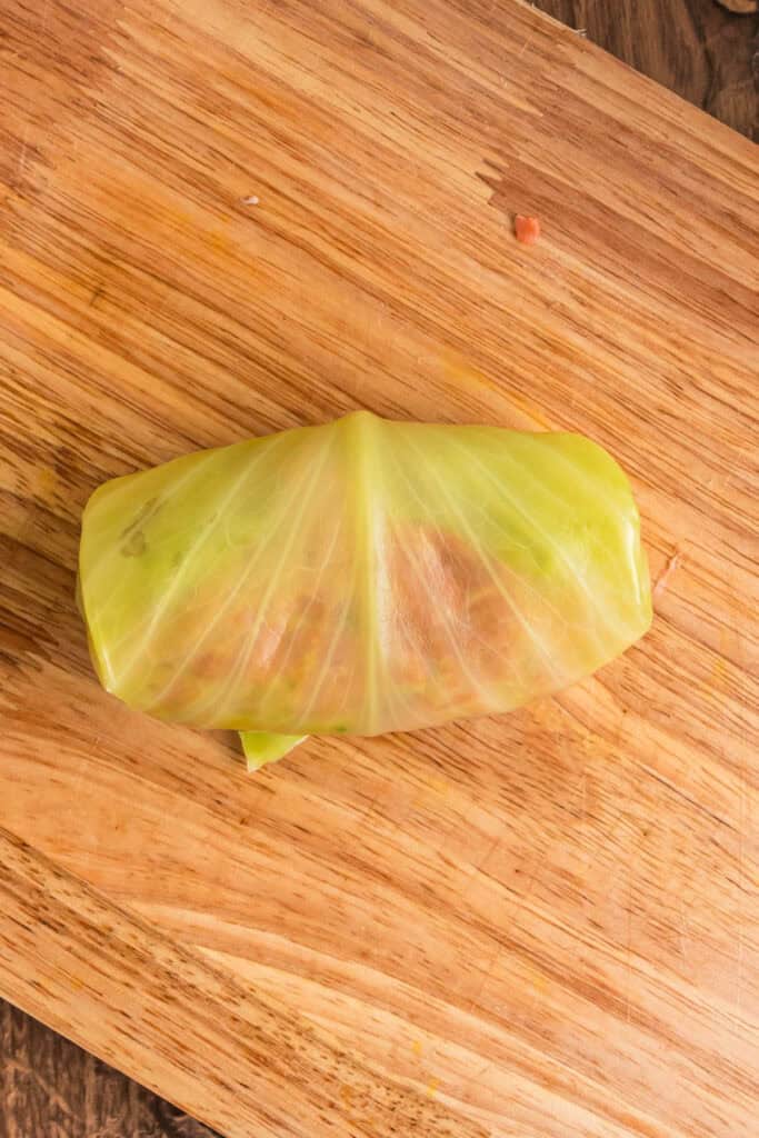 Fully rolled cabbage roll sealed and ready for baking, sitting on a wooden cutting board.
