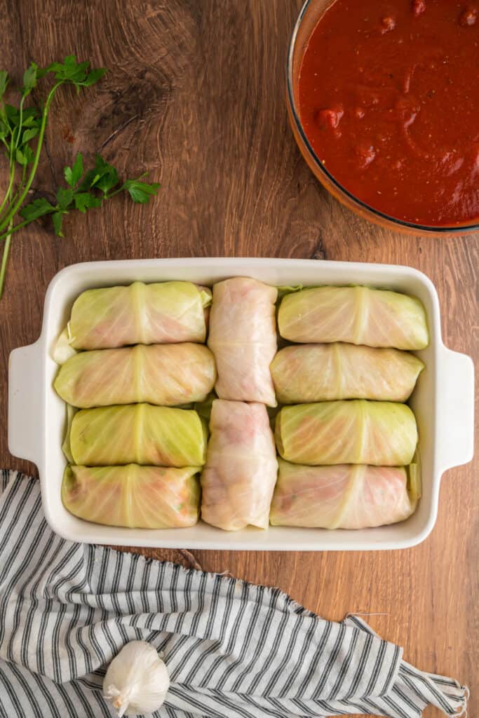 Unbaked cabbage rolls arranged neatly in a white casserole dish, ready for sauce.