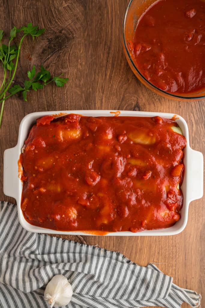 Baking dish filled with cabbage rolls completely covered in tomato sauce, ready to go in the oven.