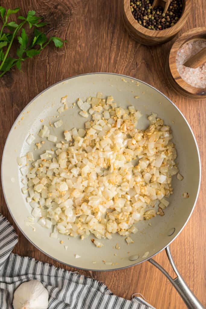 Sautéed onions and garlic in a skillet, softened and lightly golden brown, ready for the filling mixture.