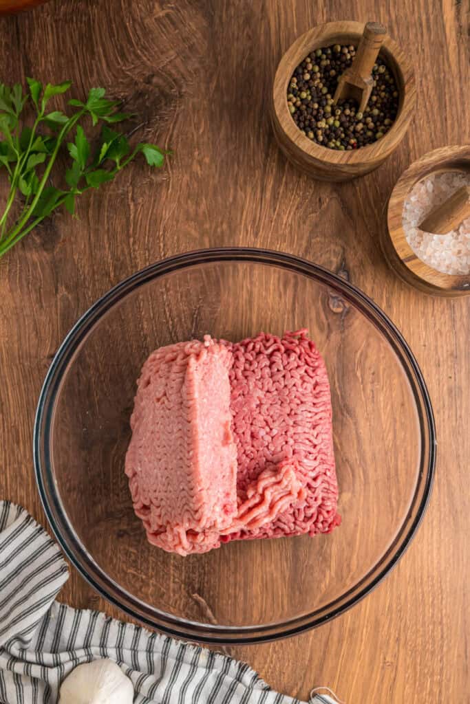 Glass mixing bowl with raw ground beef and ground pork placed side by side before mixing.
