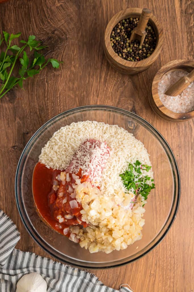 Ground meat, rice, sautéed onions, parsley, and sauce combined in a mixing bowl, ready to be stirred together.